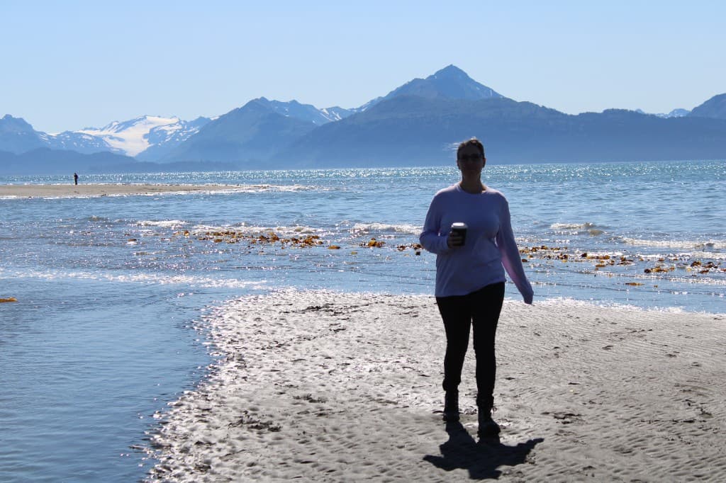 Amber, the founder of Eat it All, standing on a beach with coffee in hand and mountains in the background.